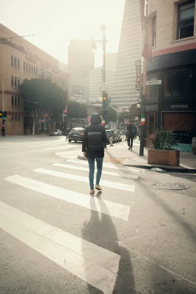 Person walking across a city crosswalk in soft morning light